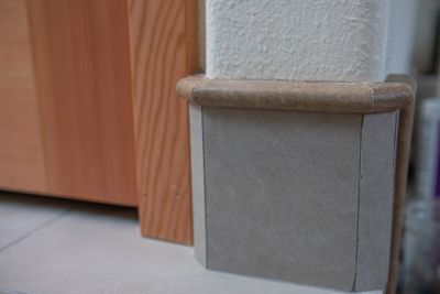 Corner protector on wall, tan and gray, near wooden cabinet.