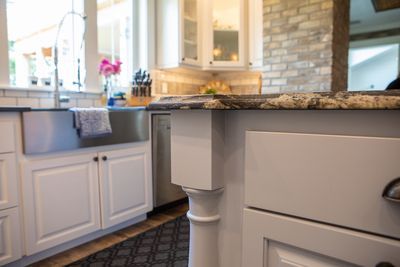 White kitchen cabinets with granite countertops, stainless steel sink, and brick accent wall.