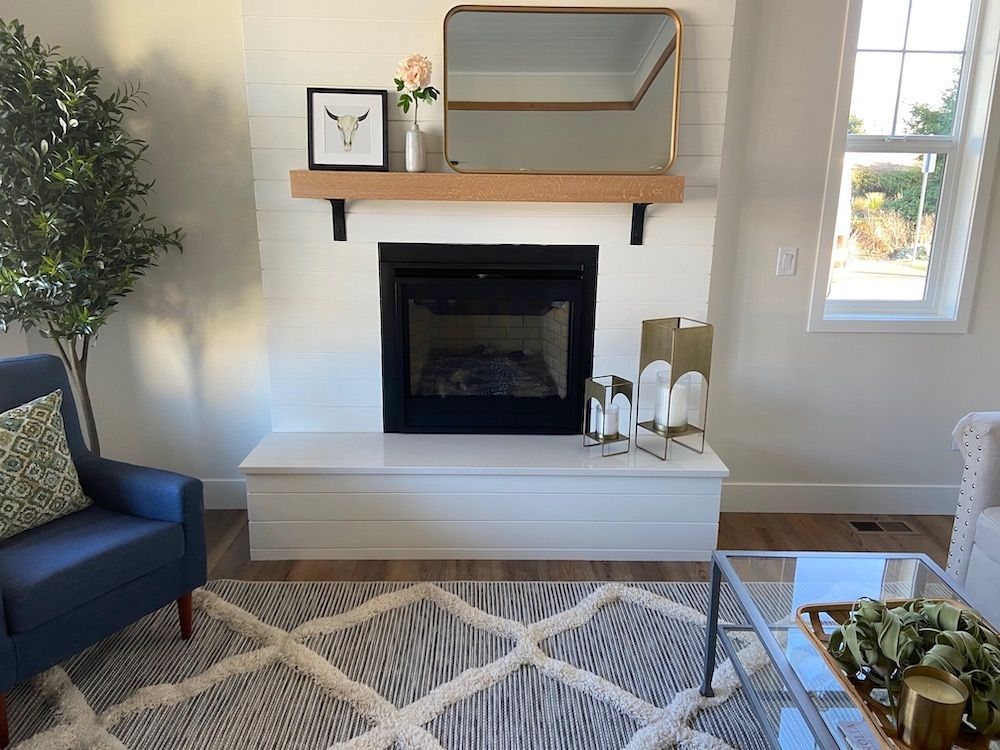 Living room with white fireplace, wooden mantle, gold mirror, blue chair, and patterned rug.