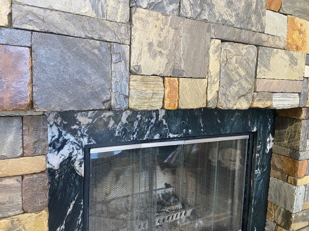 Stone fireplace with black marble trim around the firebox, with metal mesh screen.