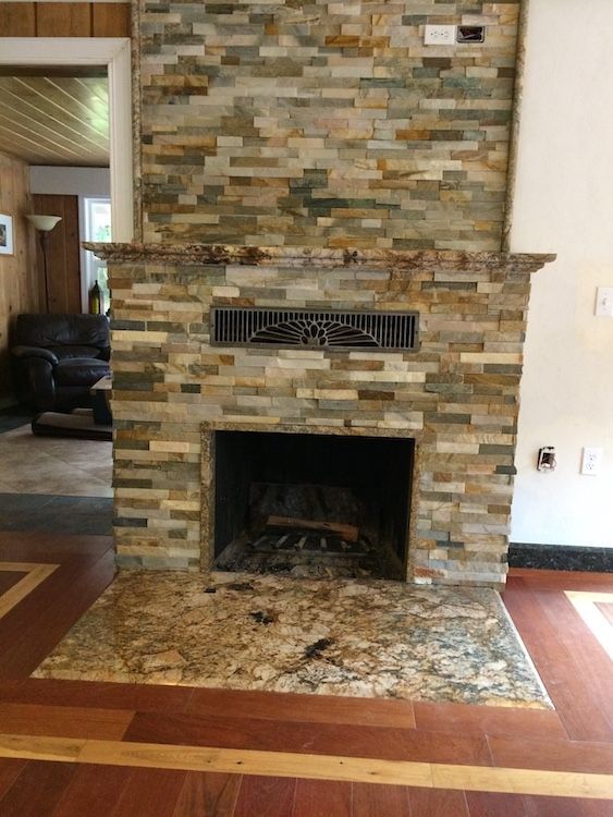 Fireplace with stacked stone facade and granite hearth, in a room with wood flooring.