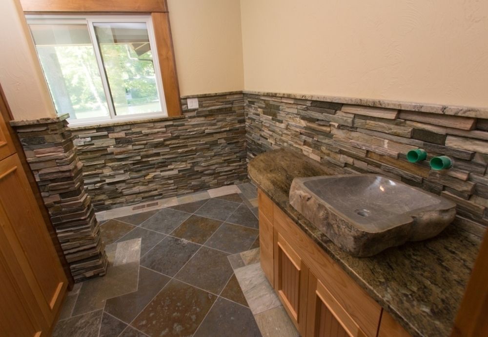 Bathroom with stone accent walls, stone vessel sink, wooden cabinet, and multi-colored slate floor.