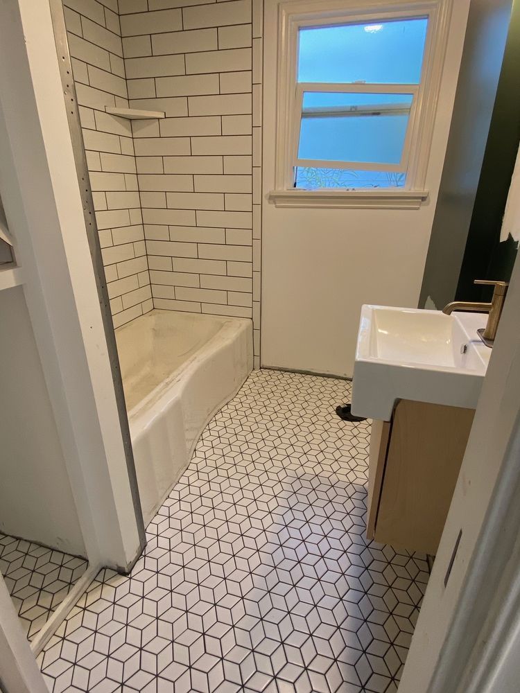 Bathroom with white subway tile shower, geometric floor tiles, and a white sink.
