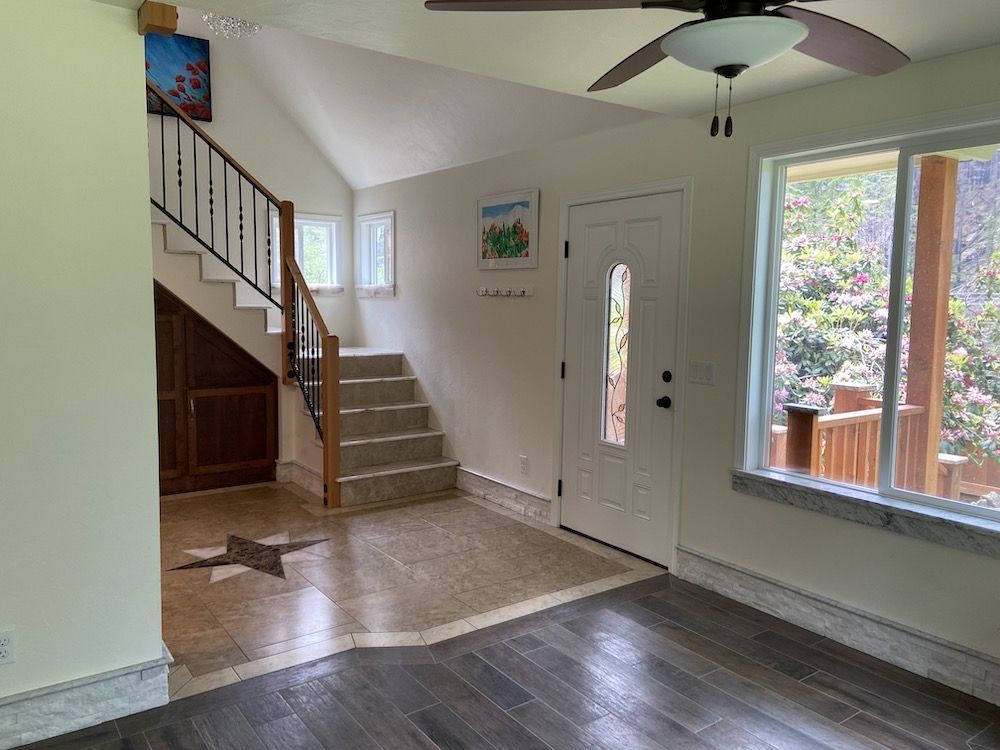Interior view of a home entrance with stairs, white door, and large window overlooking greenery.