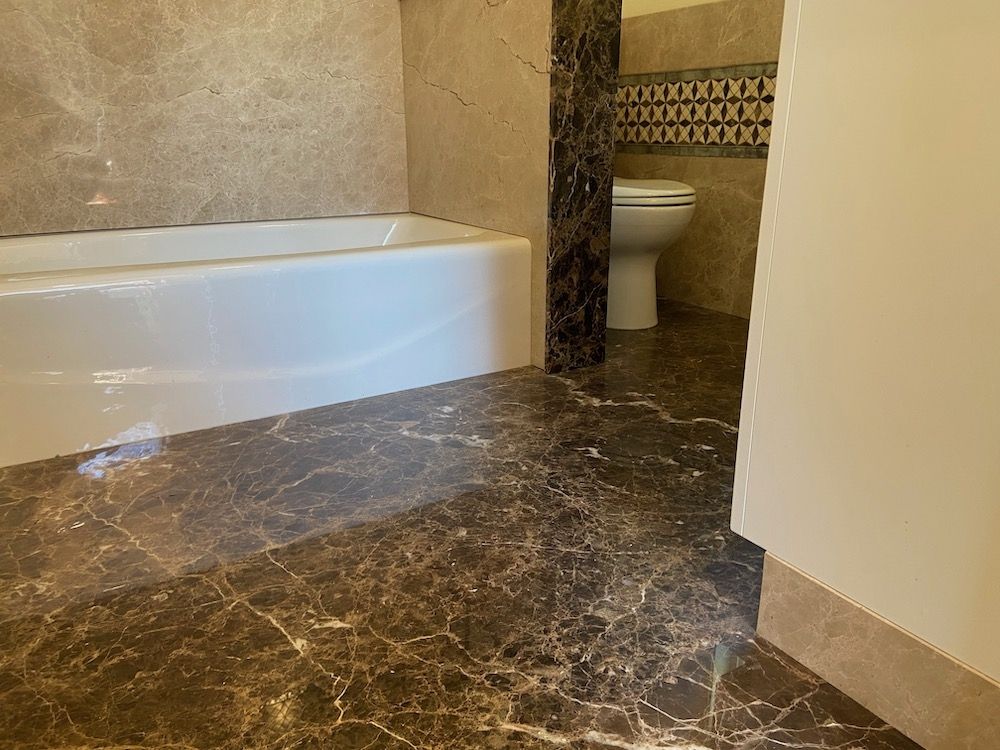 Bathroom with brown marble floor and walls, white bathtub and toilet, neutral colors.