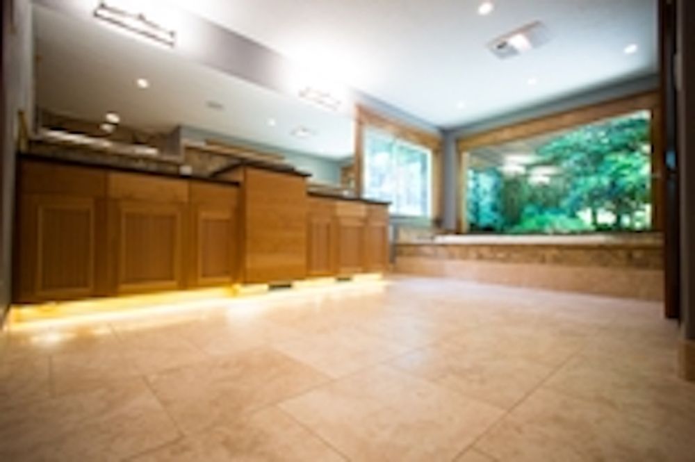 Empty room with light-colored tile floors and a wooden counter with under-cabinet lighting. Large window shows outside trees.