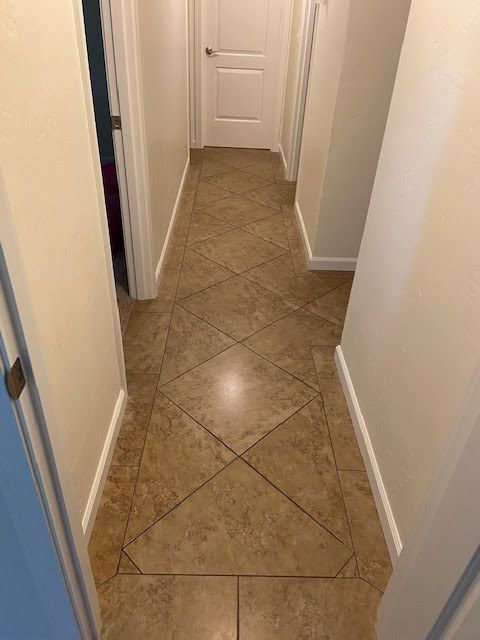 Hallway with tan tile floor and white walls, leading to a closed white door.