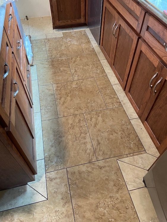 Kitchen floor with brown tiles between wood cabinets.