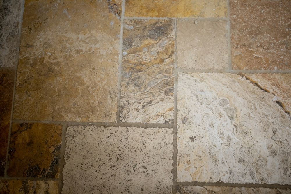 Close-up of a tiled floor made of various shades of beige and brown stone.