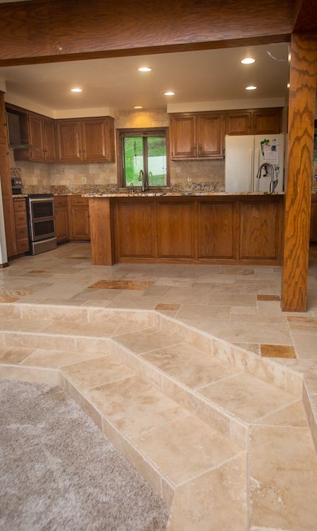 Kitchen with wooden cabinets, tile floor, and three steps leading up to the kitchen area.