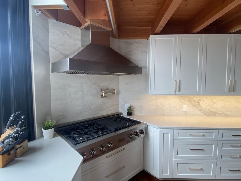 Modern kitchen with white cabinets, stainless steel stove, and copper range hood.