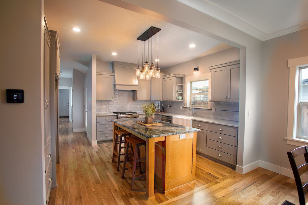 Modern kitchen with gray cabinets, wood floors, and island with pendant lights.