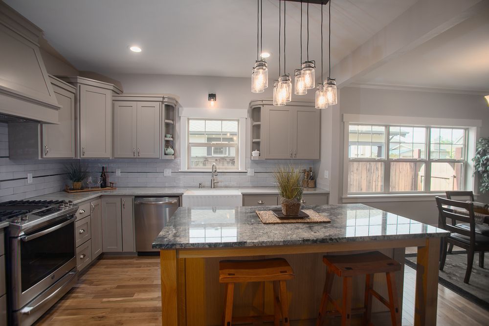Kitchen with gray cabinets, island with granite countertop, wooden stools, pendant lights.