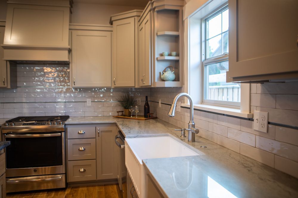 Light-colored kitchen with gray cabinets, stainless steel appliances, and white farmhouse sink.