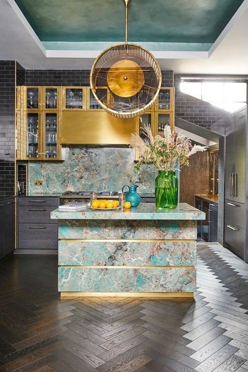 Luxurious kitchen with teal marble island, brass accents, and dark wood floor.