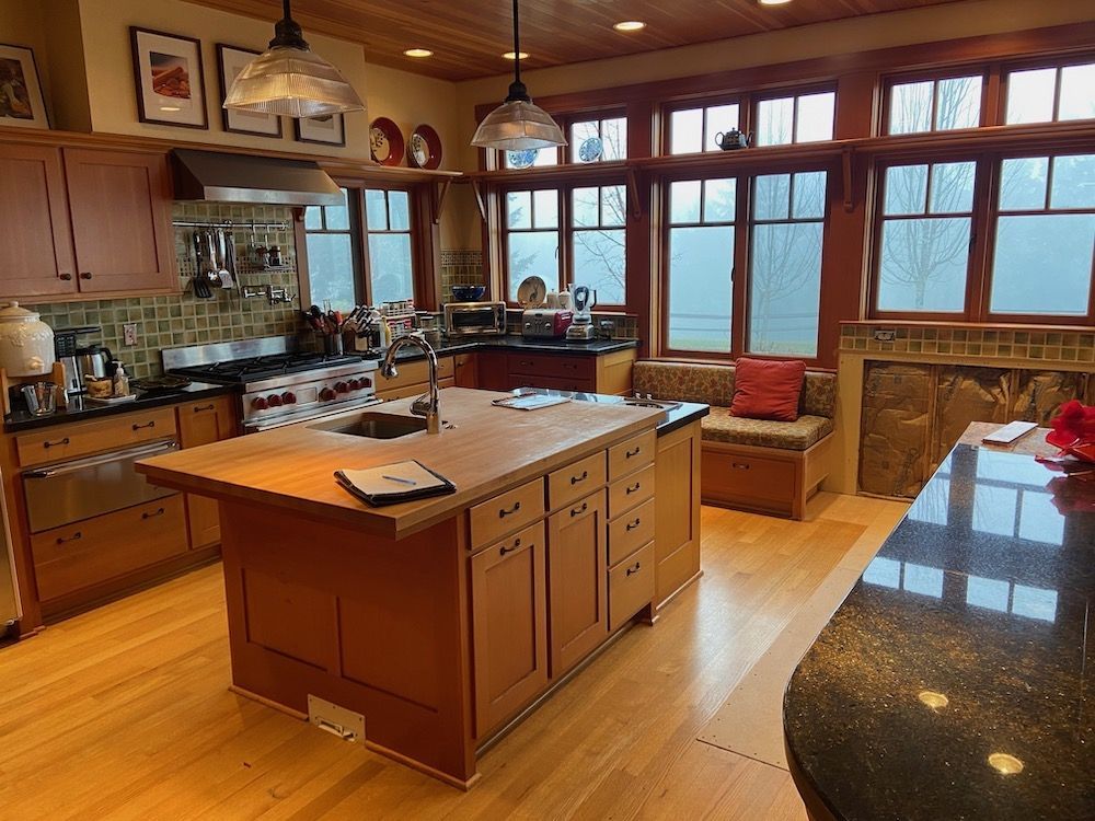 A well-lit kitchen with a large wooden island, wooden cabinets, and large windows with a bench.