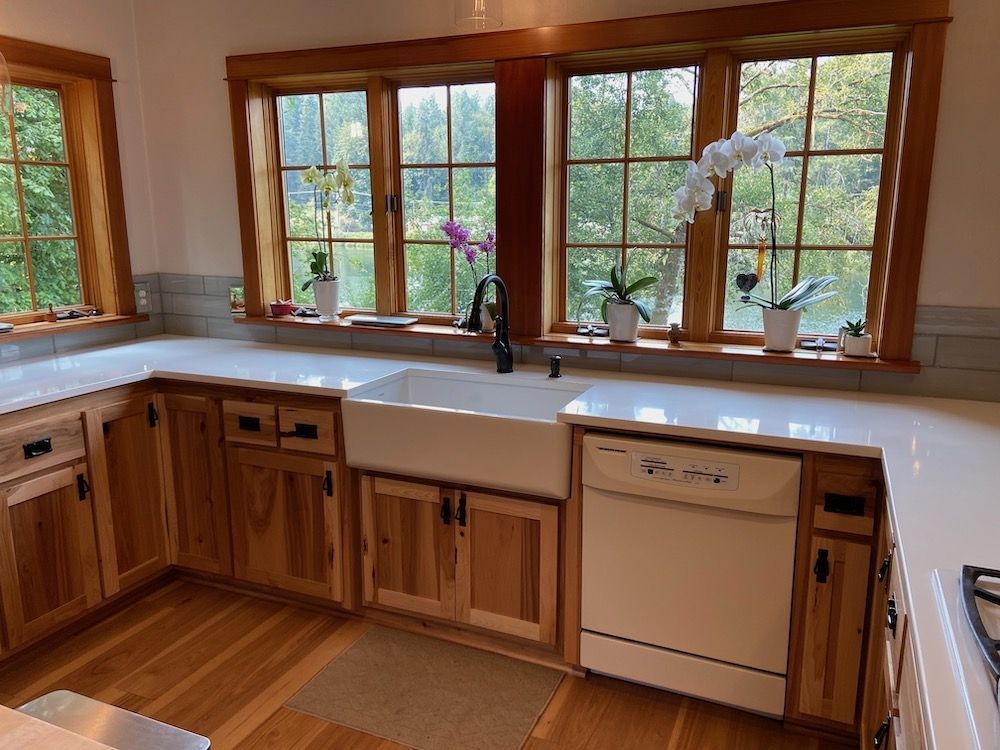 Kitchen with light wood cabinets, white countertops, farmhouse sink, and large windows with orchids.