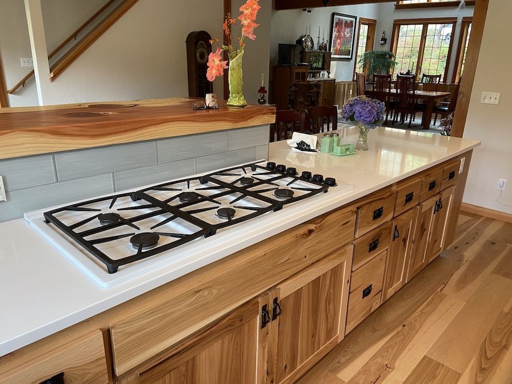 Kitchen island with a gas cooktop, light wood cabinets, and white countertop.