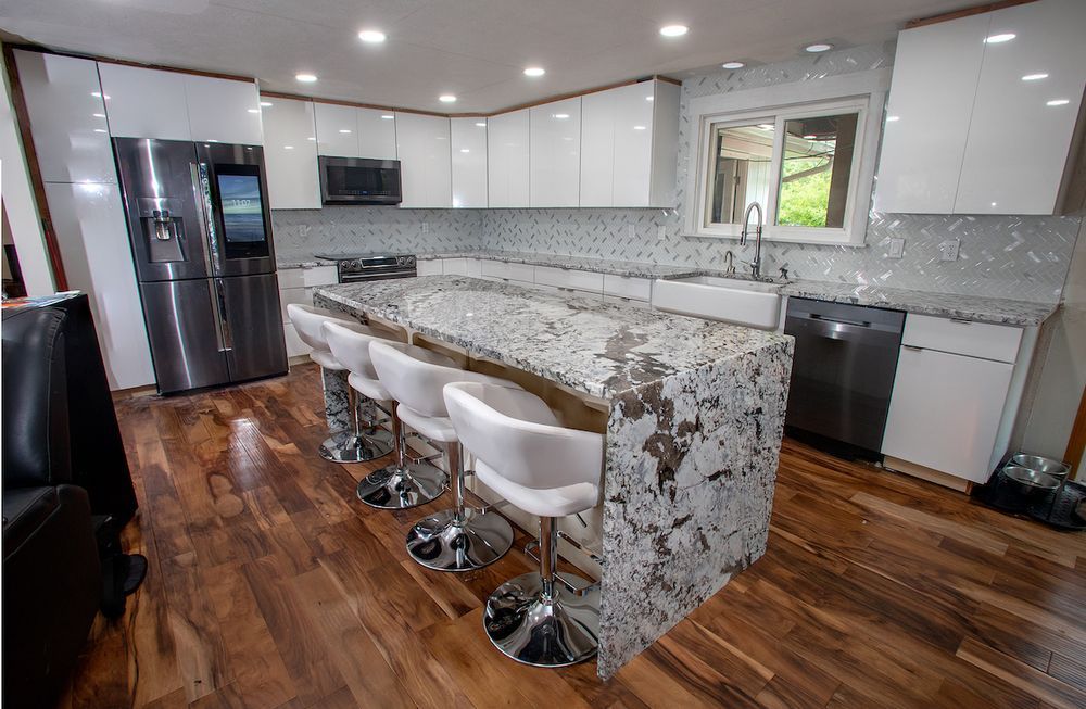Modern white kitchen with a large island, stainless steel appliances, and wood flooring.