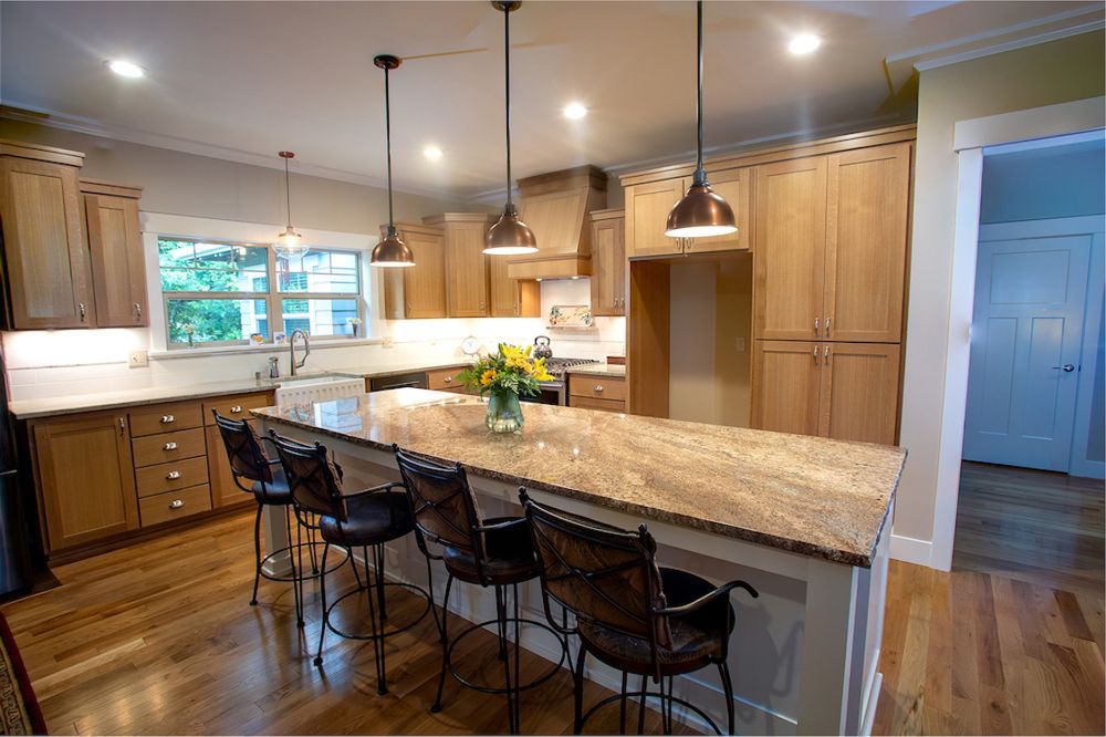 Modern kitchen with light wood cabinets, granite island, and bar stools.