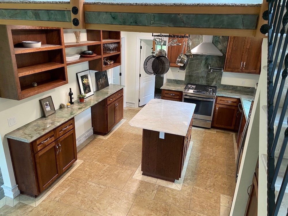 Kitchen with brown cabinets, island, and granite countertops. Light brown tile floor.