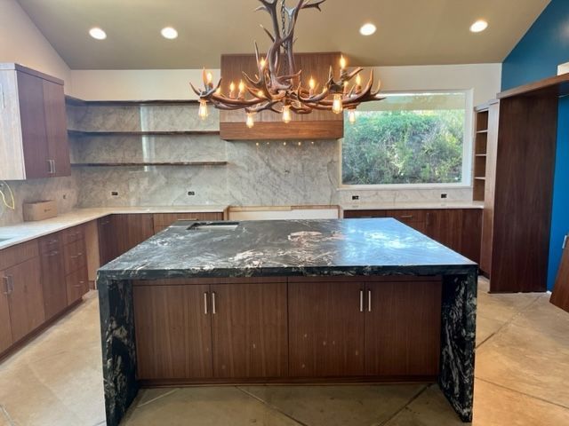 Kitchen with brown cabinets, island, and antler chandelier. White marble backsplash and countertops.