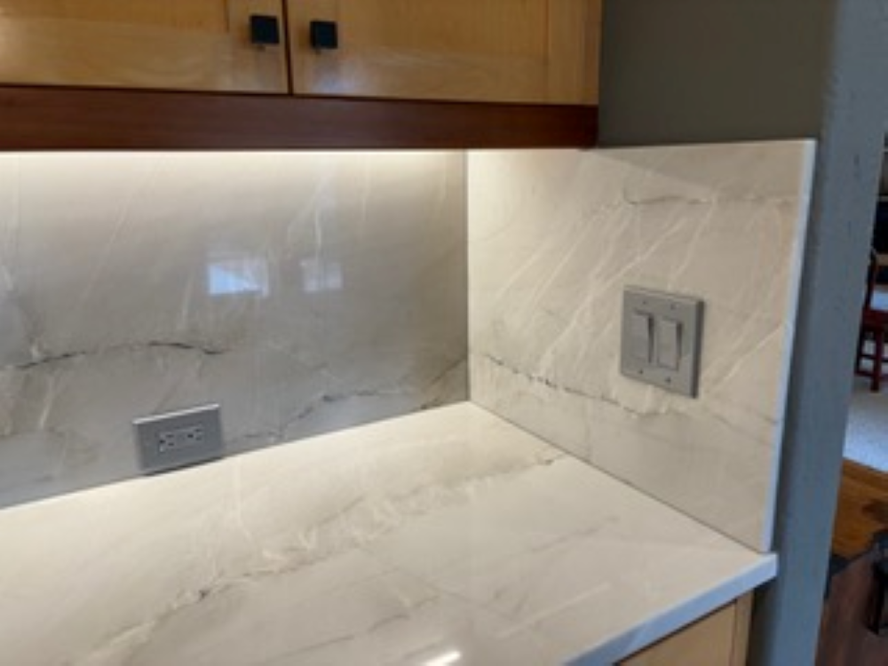 White marble kitchen countertop and backsplash with recessed lighting and light switches.