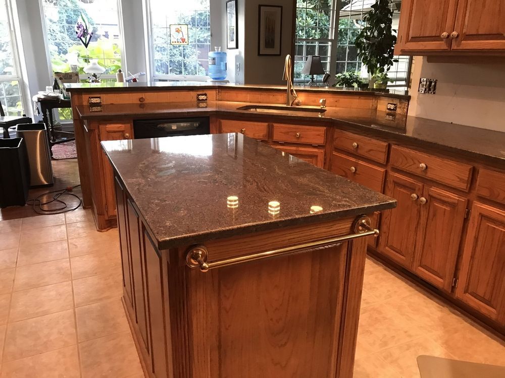 A kitchen with wooden cabinets and countertops. An island with a granite top and towel bar.