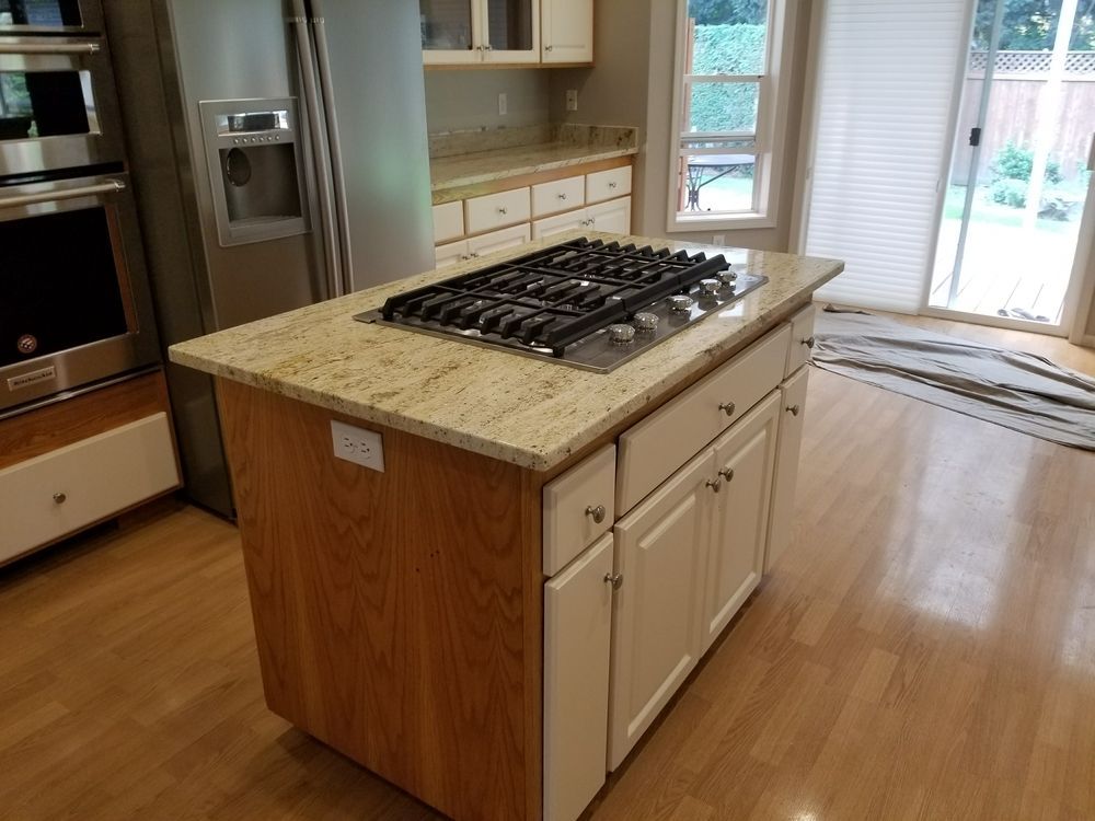 Kitchen island with stovetop, granite countertop, white cabinets, and wooden side panel.