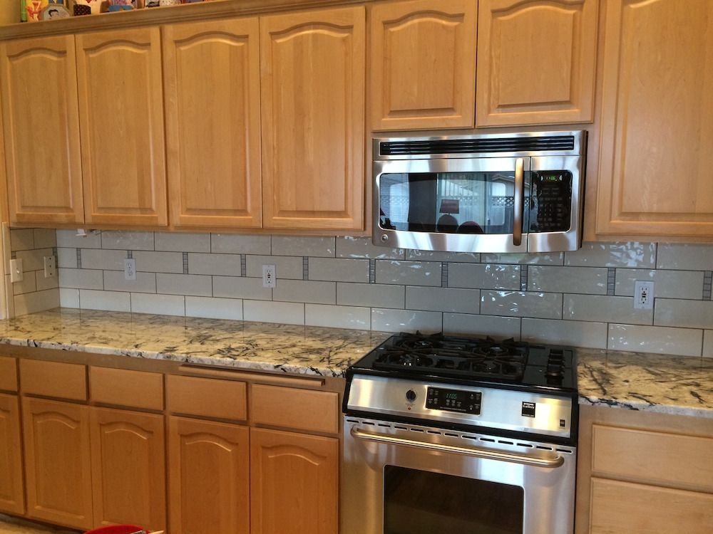 Kitchen with light wood cabinets, granite countertops, stainless steel appliances, and beige backsplash tiles.