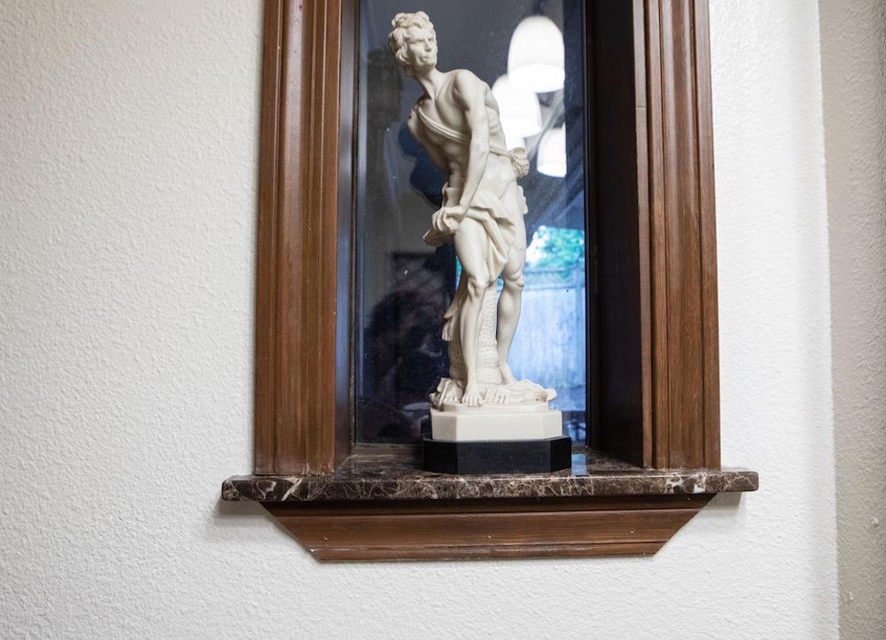 Statue in a framed alcove: a classical figure on a pedestal, set in a wood and marble niche on a white wall.