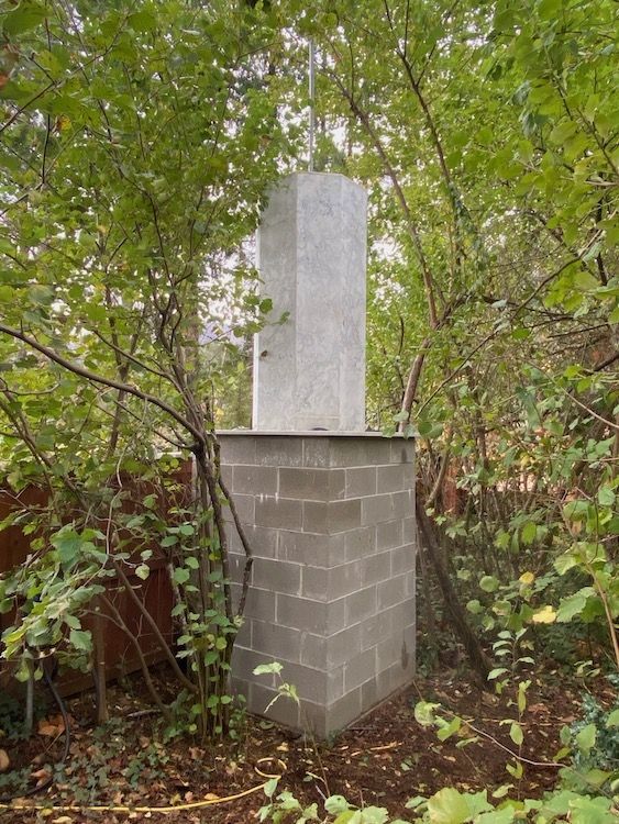 Granite obelisk on concrete block base, surrounded by trees.