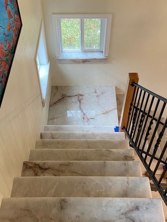 Staircase with marble-look steps leading up, window at top, and a black wrought iron railing on the right.