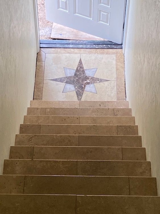 Staircase with light brown steps leading up to a tiled landing with a star design and an open white door.