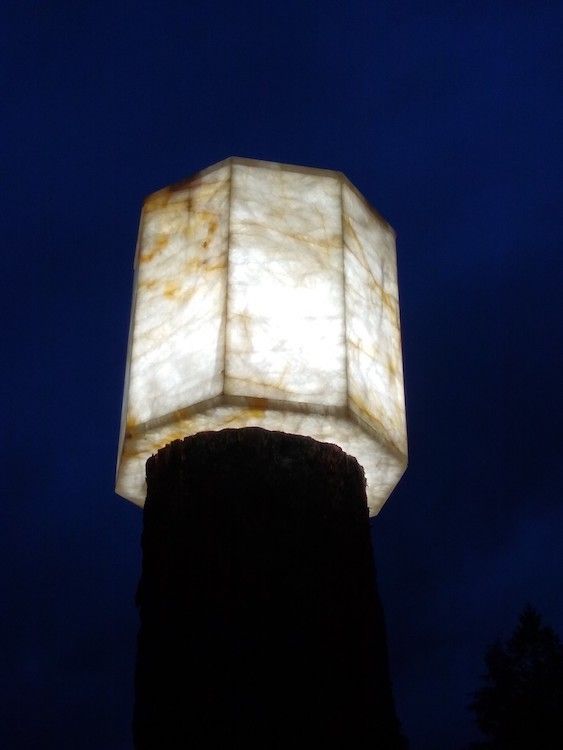 Glowing, octagonal lamp atop a dark, cylindrical structure, against a dark blue sky.