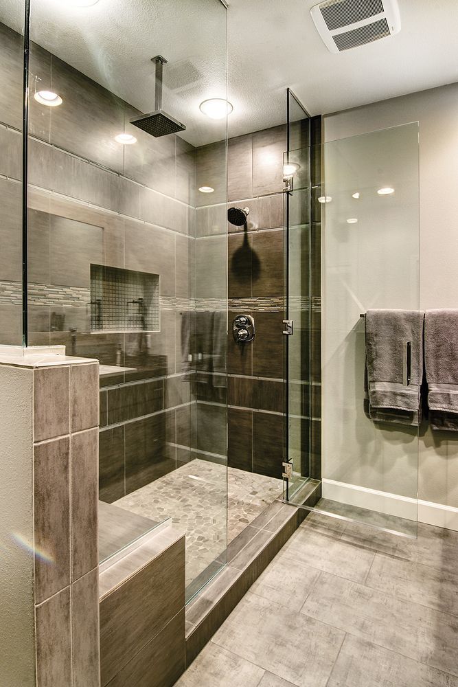 Modern bathroom with a glass shower enclosure; gray tile, stone floor, and towel rack.