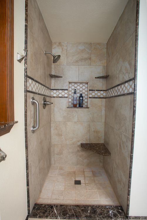 Tile shower with built-in shelves, bench, and handrail, featuring light and dark brown tile and decorative accents.