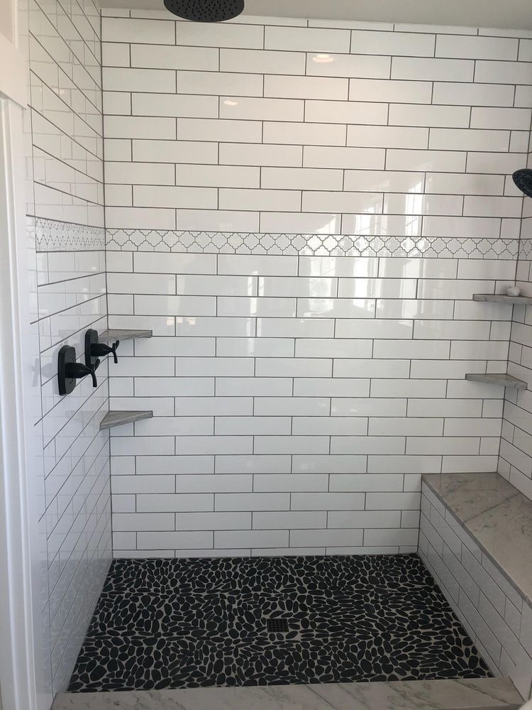 White-tiled shower with black pebble floor, built-in bench, and multiple showerheads.