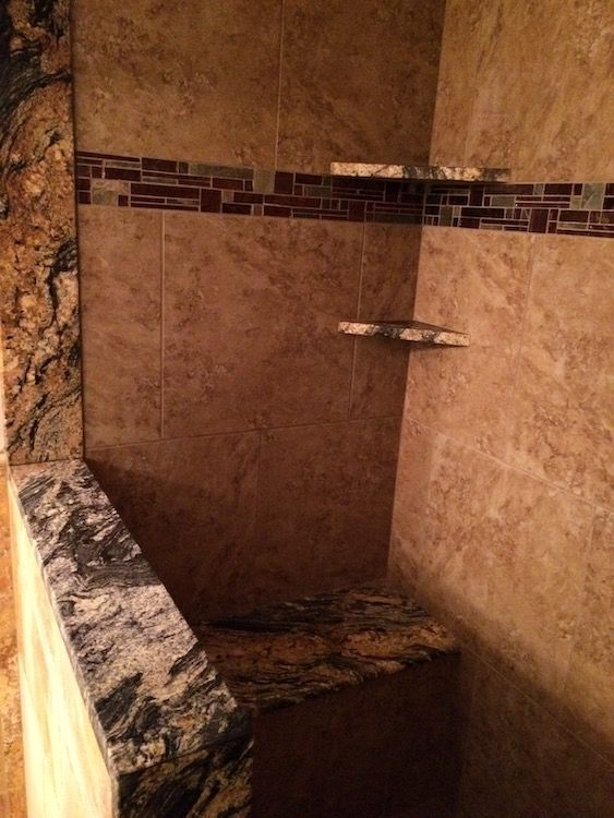 Shower with tan tile, granite ledge, and built-in shelves. Accent strip has red and brown tiles.