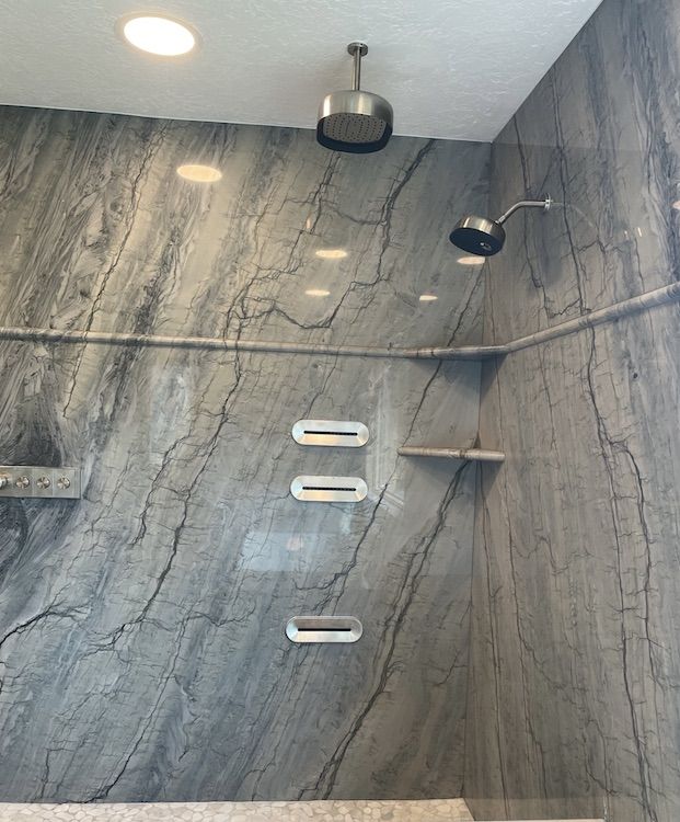 Shower with gray marble-look walls, three built-in shelves, two showerheads, and recessed lighting.
