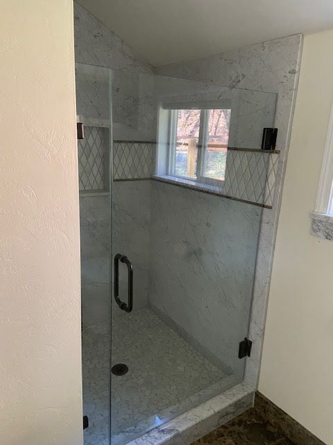 Glass shower enclosure with marble tile walls and a small window.