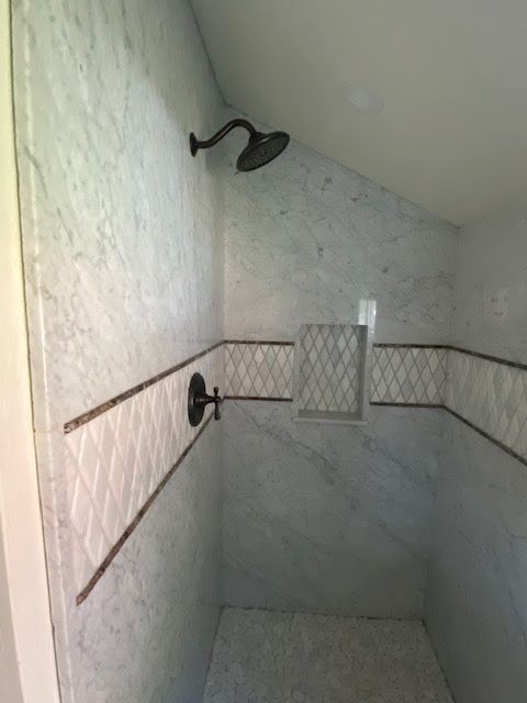 Shower with marble-like tile, dark fixtures, and decorative mosaic accent.
