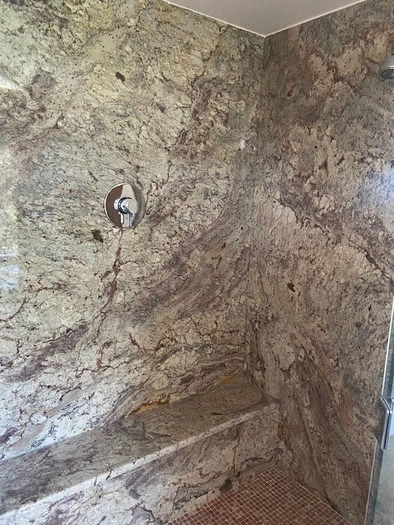 Shower with granite walls and a built-in bench. The walls are beige, brown, and gray.
