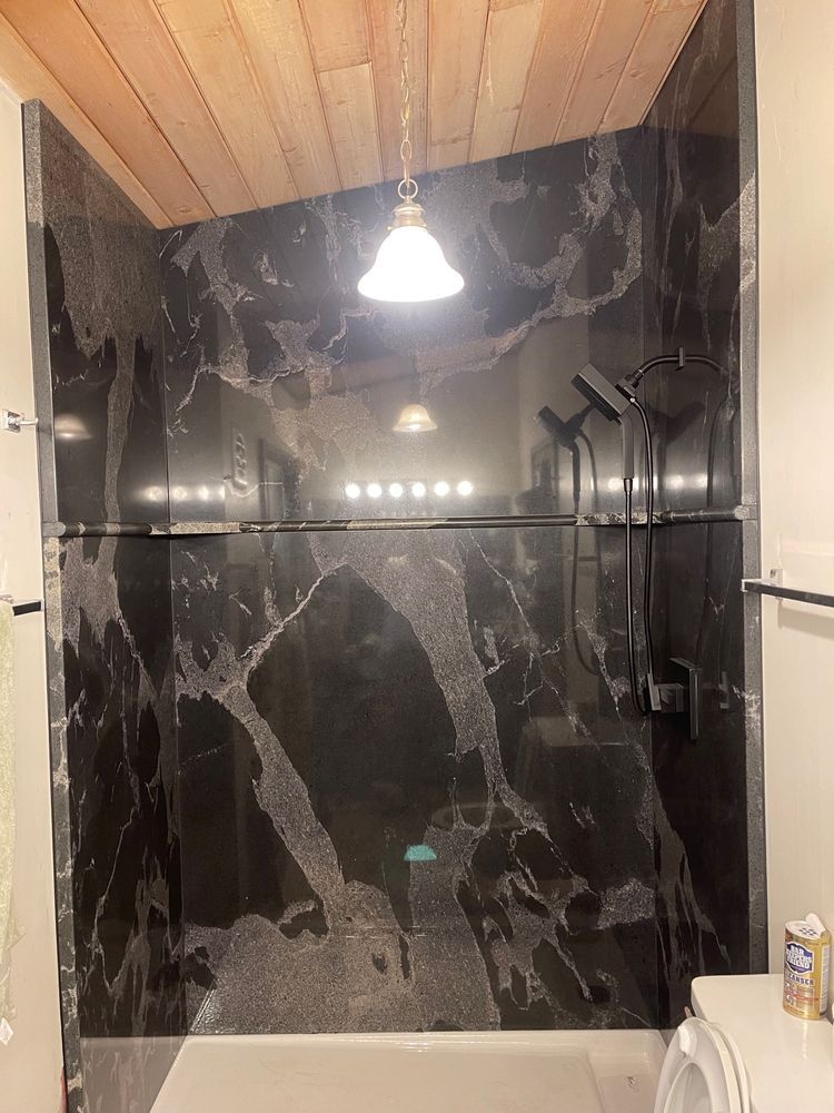 Black marble shower with wood ceiling and a single light fixture.