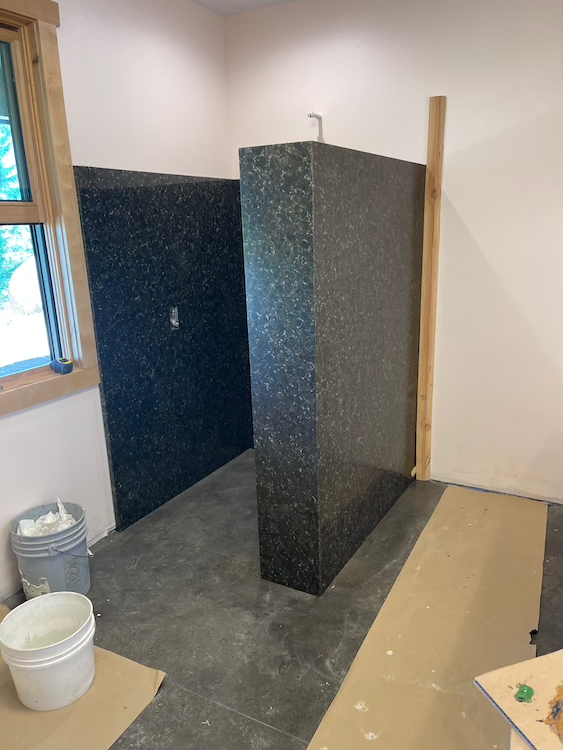 Bathroom under construction, walls of black speckled material, concrete floor, pink walls.
