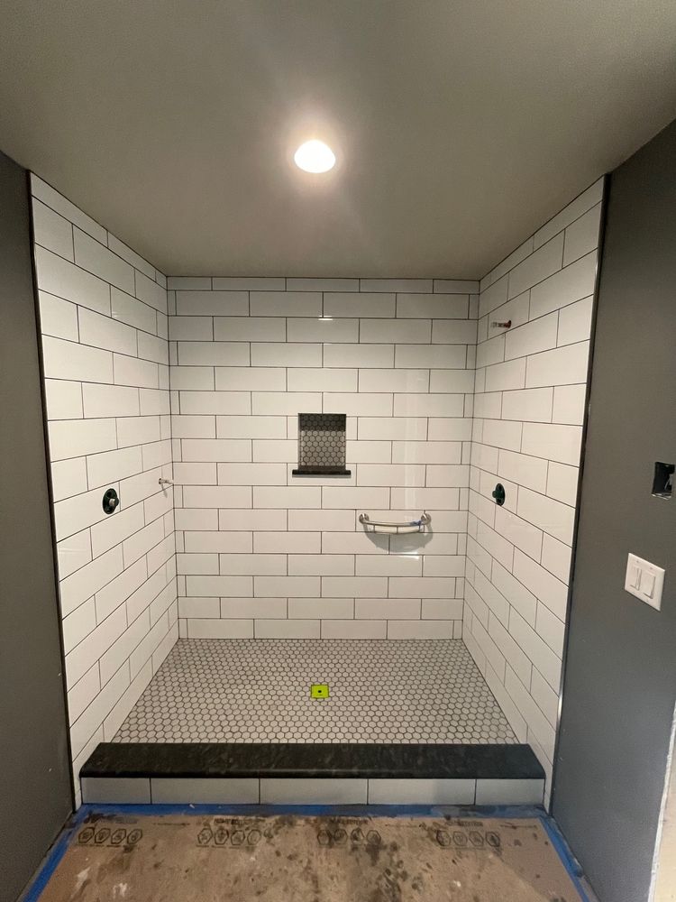 Completed shower stall with white subway tiles, black accent tiles, and a gray frame.