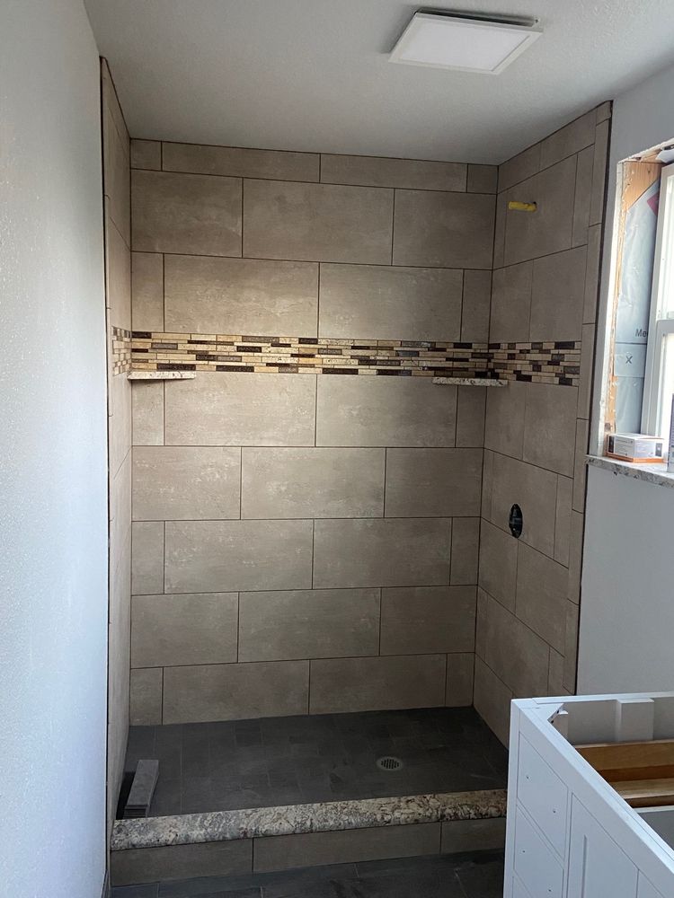 Shower stall with gray tile walls and floor, and a shelf of brown mosaic tile.