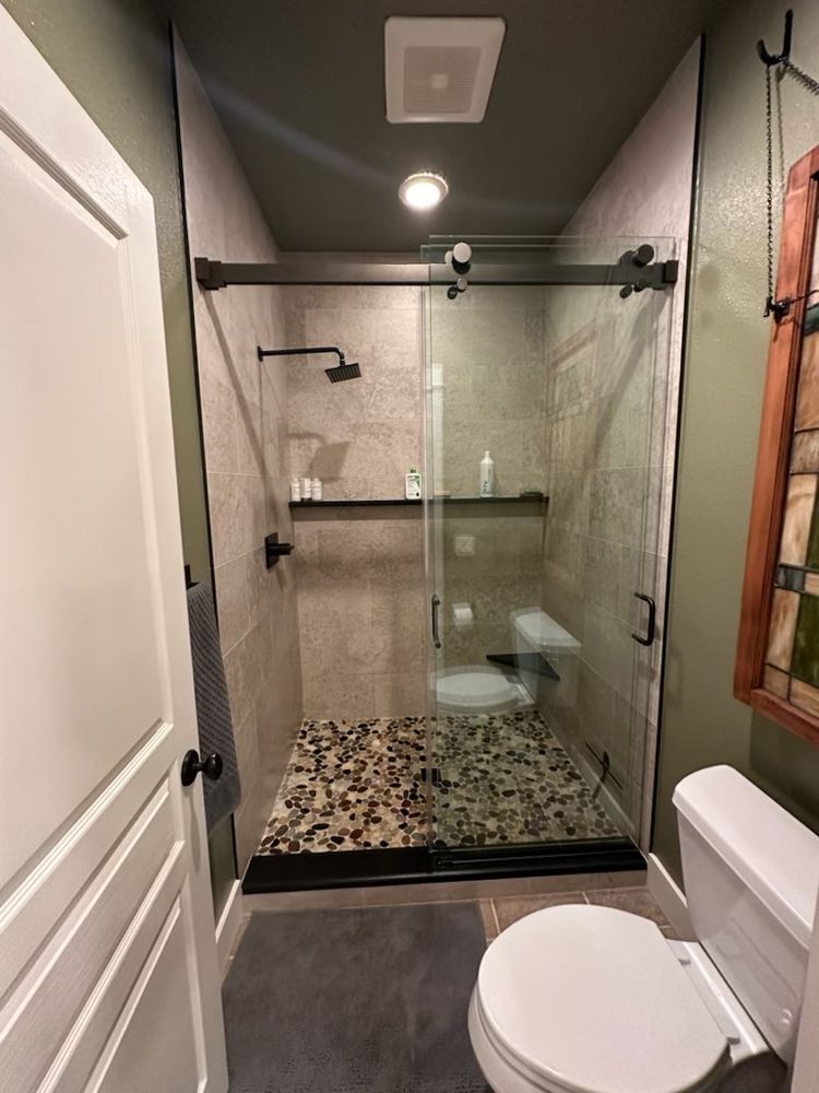 Bathroom with a shower stall featuring a pebble floor and glass sliding doors, next to a toilet.