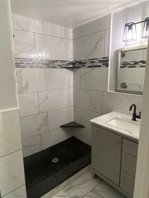 Newly remodeled bathroom with marble-look tiles, black shower floor, and a light gray vanity.