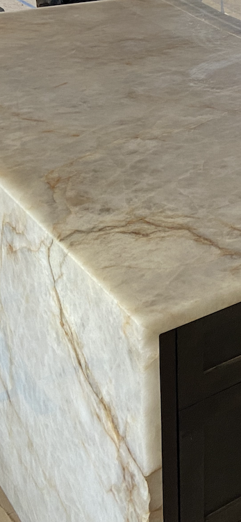 Close-up of a stone countertop with dark brown cabinets. The stone is white with brown veins and a smooth finish.